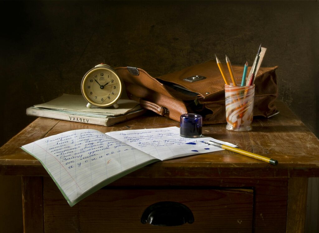 Classic wooden desk with writing materials, vintage clock, and a leather bag, ink&archives.